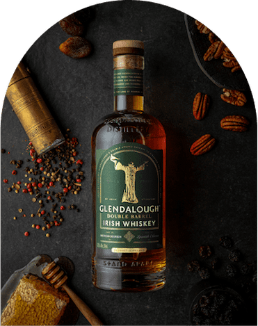 A bottle of Glendalough Double Barrel Irish Whiskey on a dark stone surface, surrounded by honeycomb, peppercorns, pecans, and dried fruit.